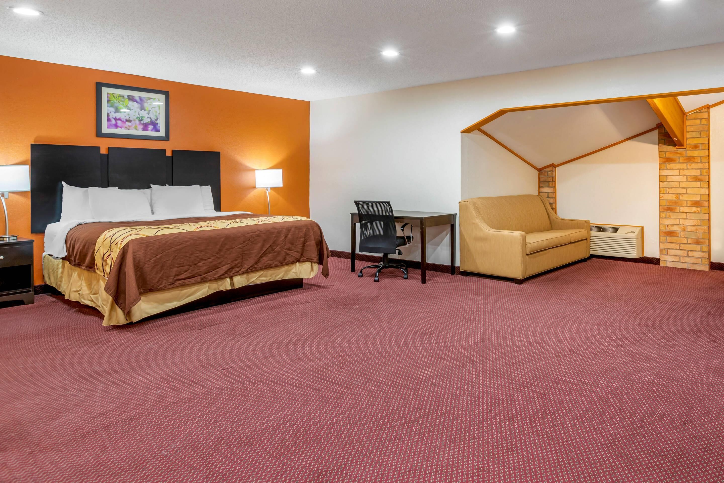 A hotel room with a bed, a desk, a chair, and a red carpet.