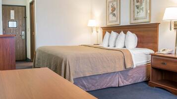 A hotel room with a bed, bedside lamps, a wooden headboard, a desk, and a door.