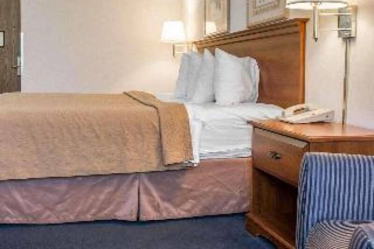 A hotel room with a bed, bedside lamp, and a wooden nightstand.