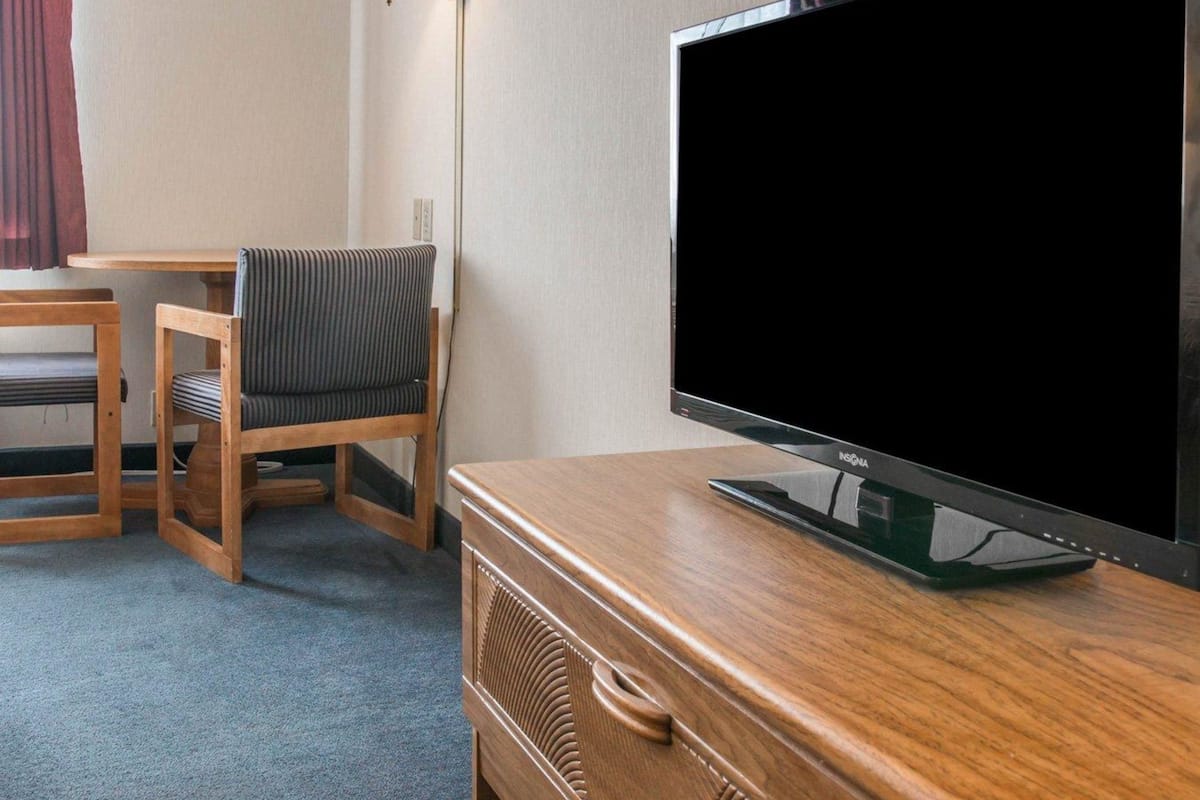 A hotel room with a wooden desk, a television on a wooden stand, a striped chair, and a floor lamp.