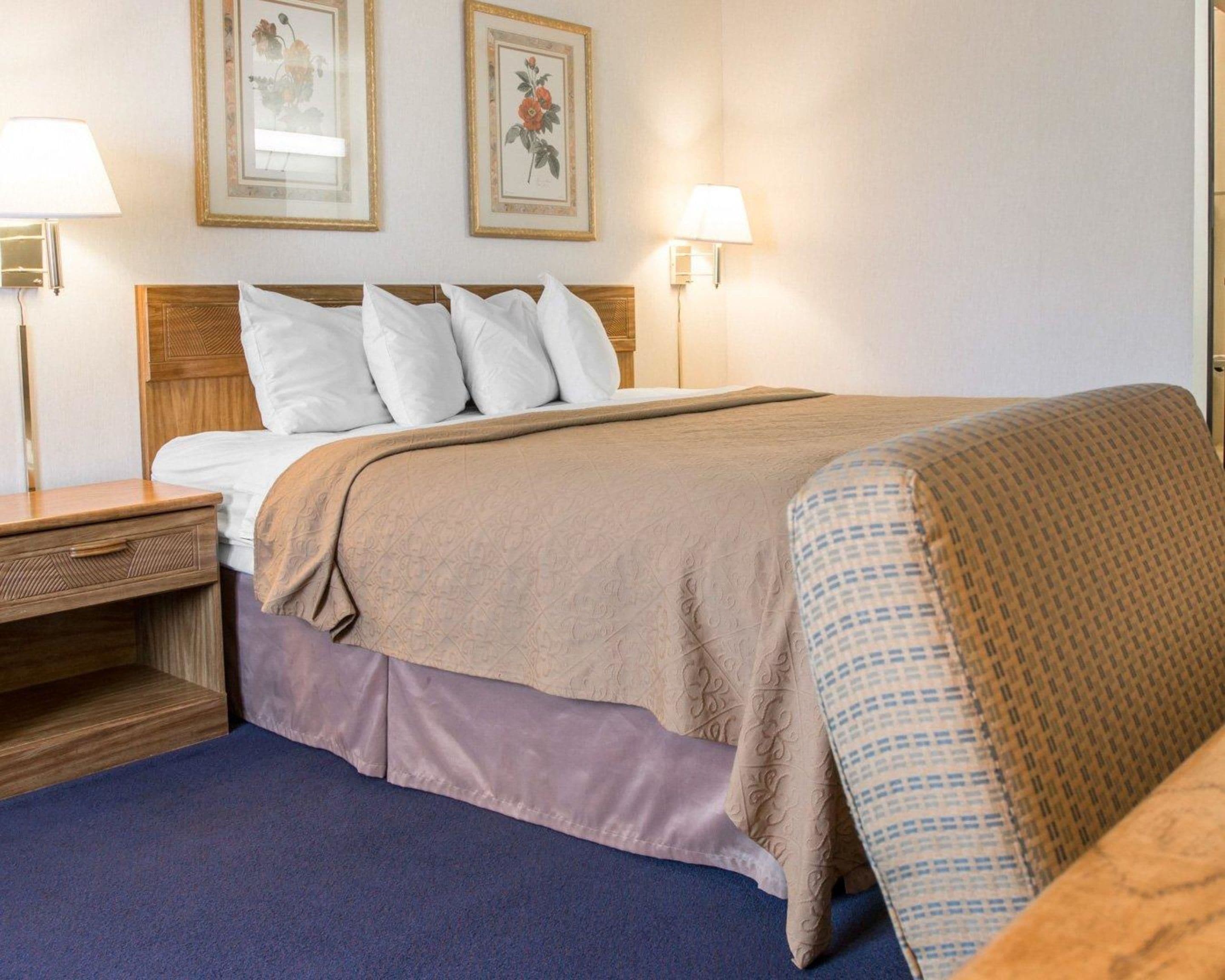 A neatly made bed with a beige blanket and pillows, a wooden nightstand with a lamp, and two framed floral pictures on the wall.