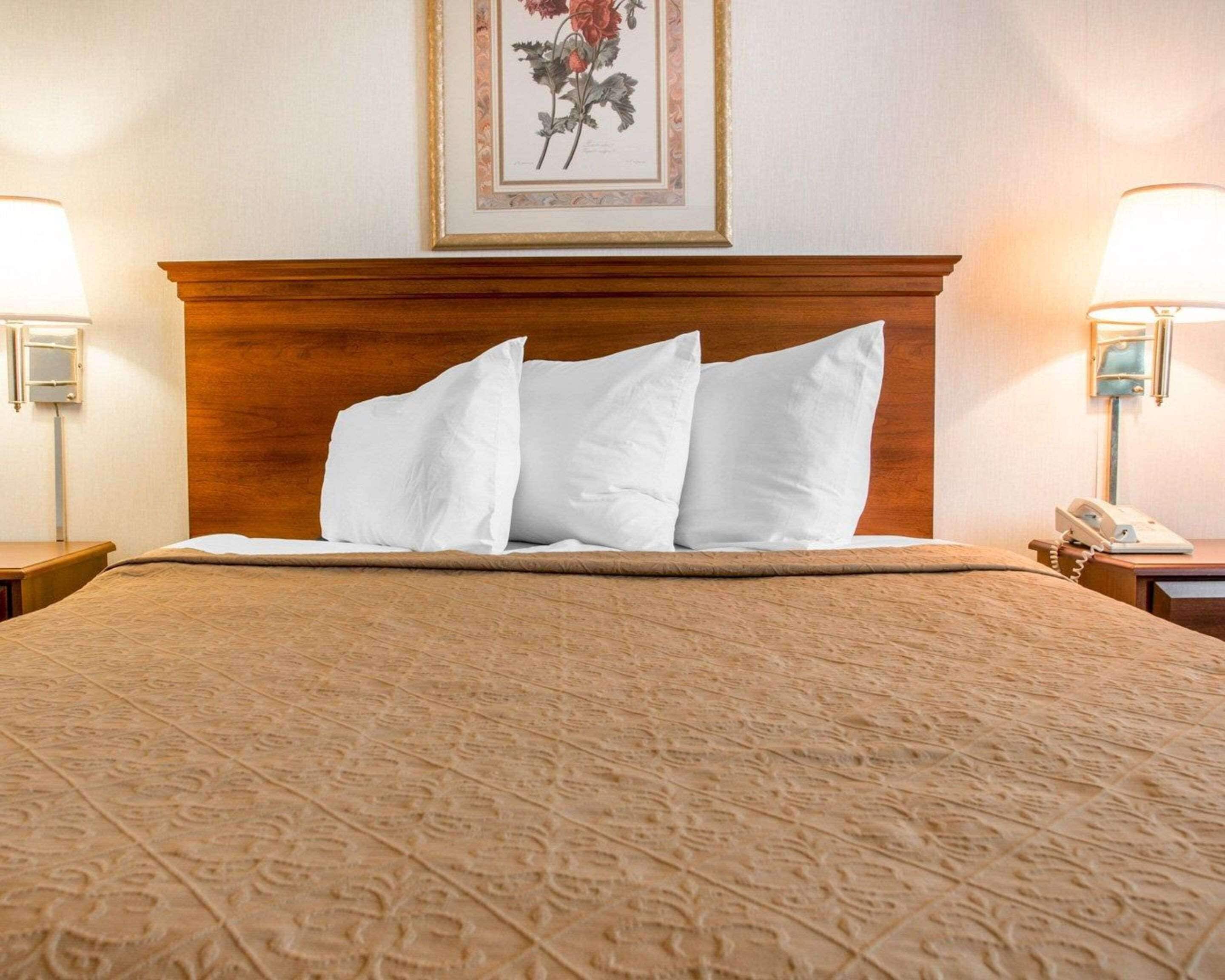 A neatly made bed with a patterned bedspread, a wooden headboard, and a framed floral artwork above it.