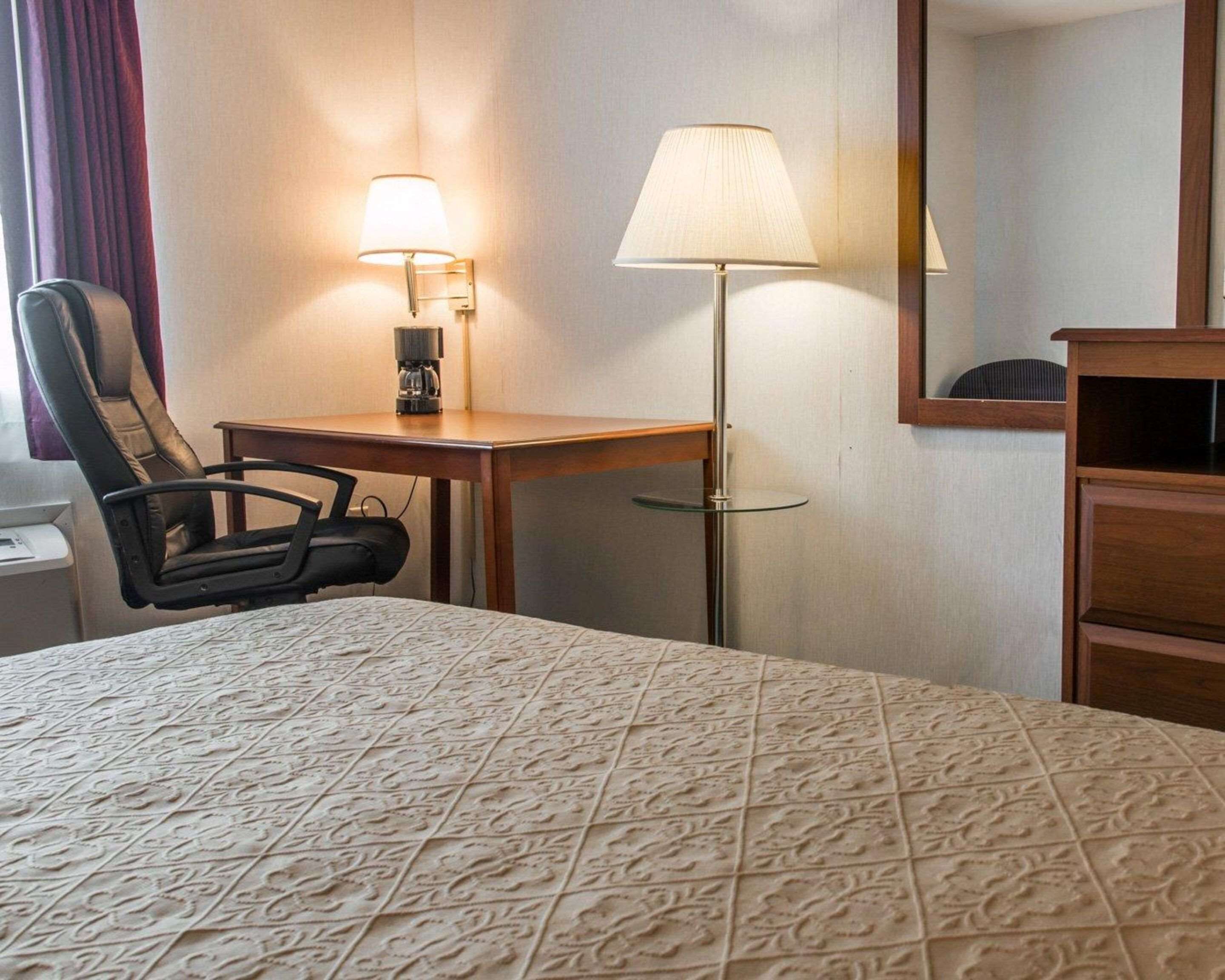 A hotel room with a bed, a desk, a chair, a lamp, and a mirror.