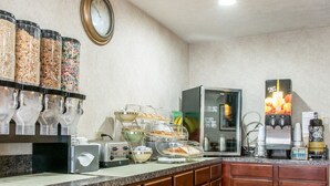 Ein Frühstücksbuffet mit Getreide, Obst und Saftspendern, einer Kaffeemaschine und einem Toaster.