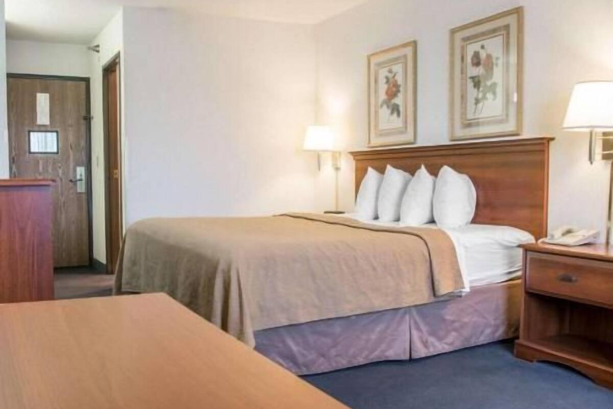 A hotel room with a bed, bedside tables, a desk, and framed pictures on the wall.
