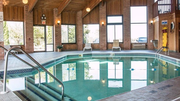 Ein Hallenbad mit Holzbalkendecke und Backsteinwänden, umgeben von Fenstern und einigen Liegestühlen.