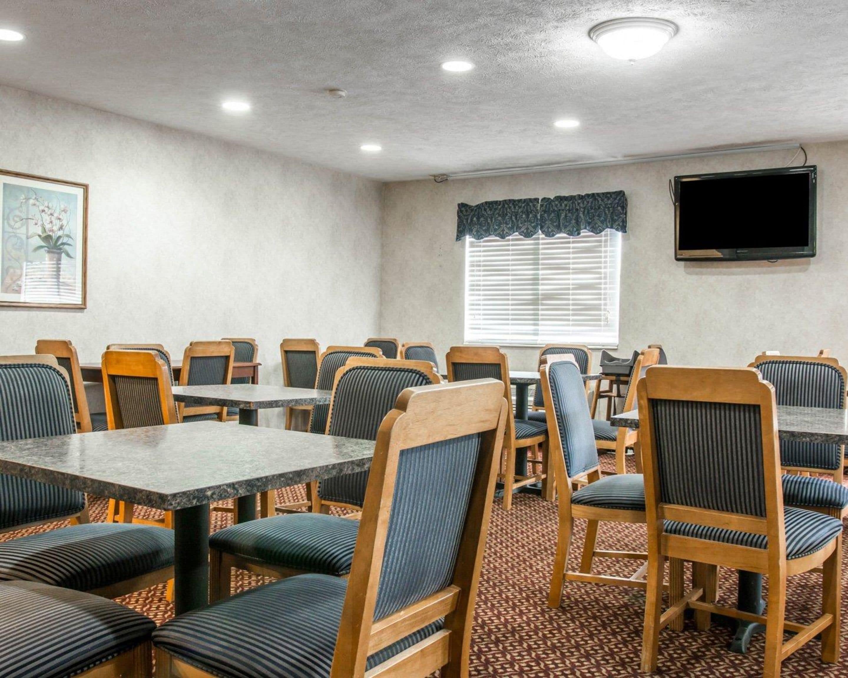 A conference room with wooden tables and chairs, a patterned carpet, a television on the wall, and a window with blinds.