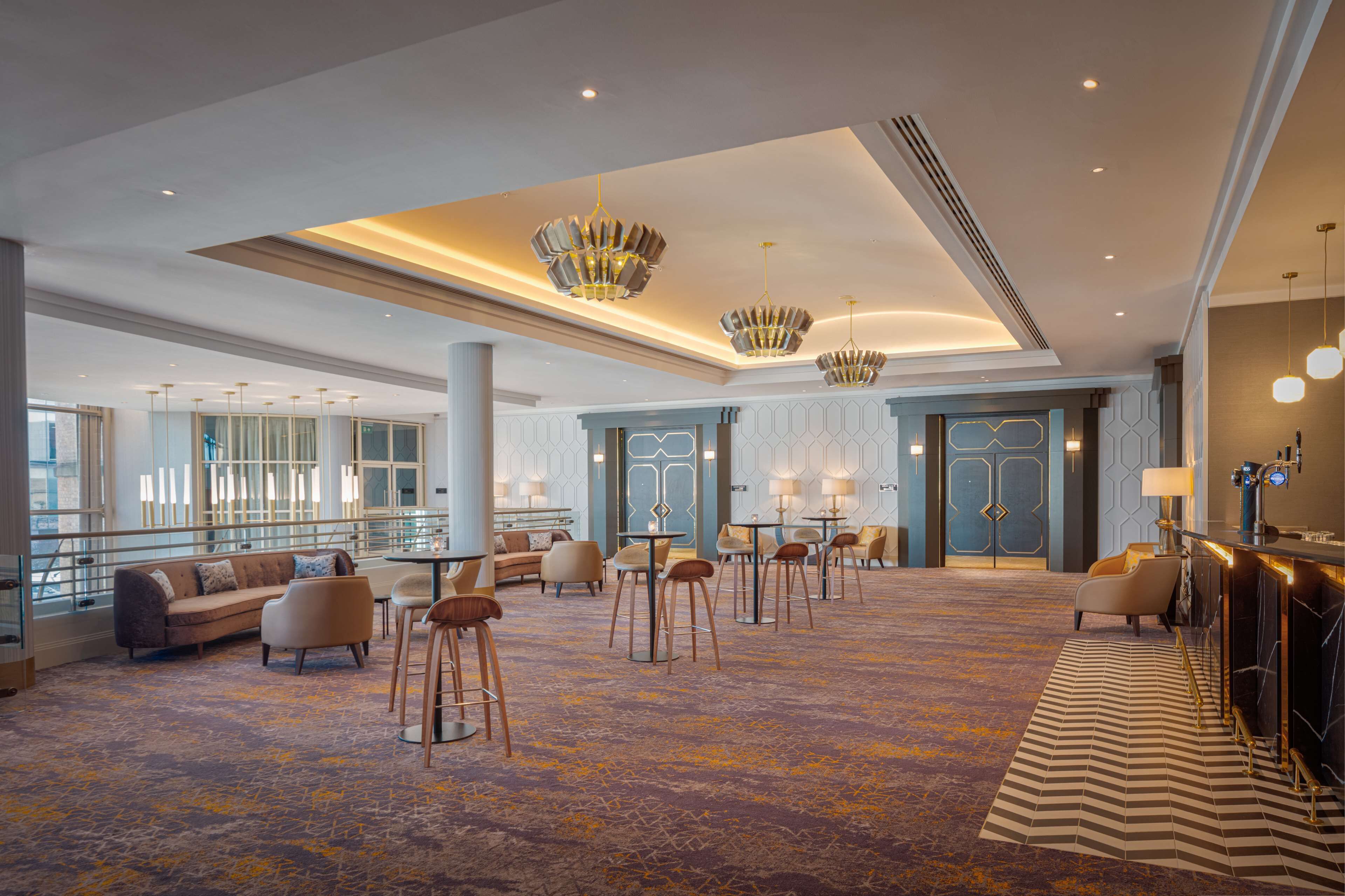 A spacious lobby with high ceilings, modern chandeliers, and a mix of seating arrangements including sofas and bar stools.