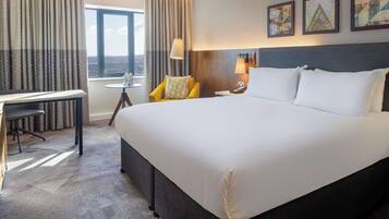 A hotel room with a large bed, a desk, a chair, a lamp, and a window with curtains.