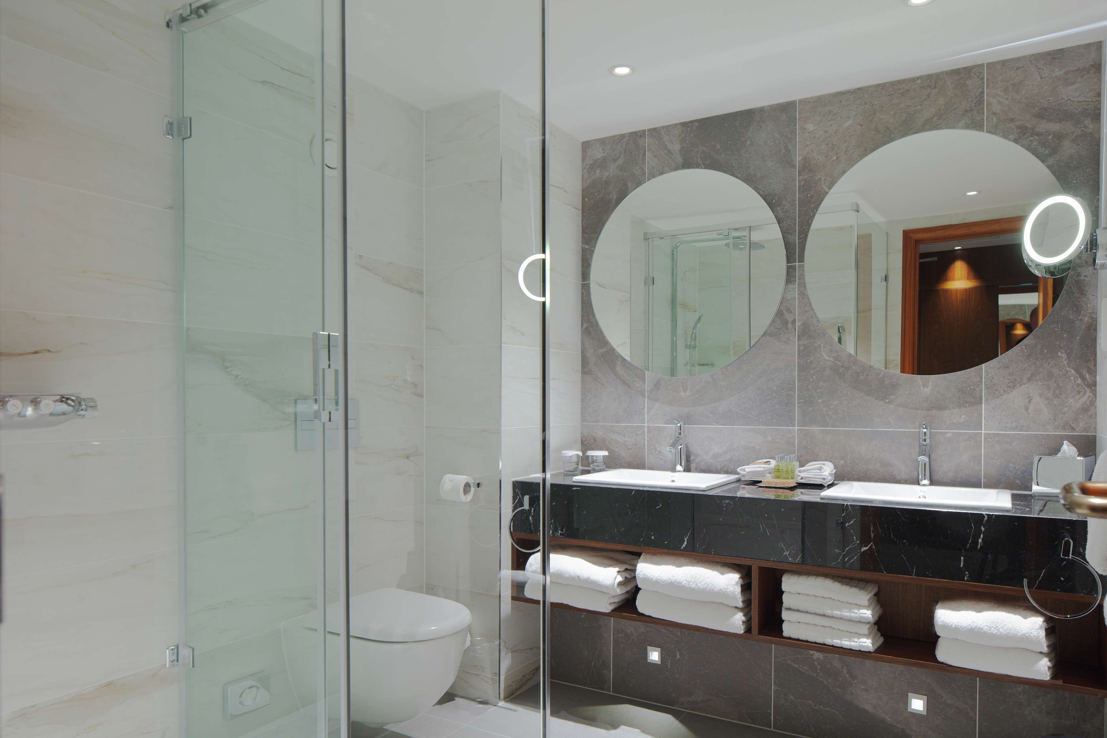 Un baño moderno con cabina de ducha de vidrio, inodoro, lavamanos con espejo y perchero para toallas.