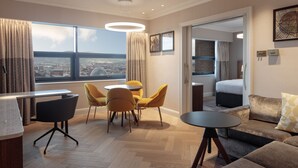 A modern hotel room with a dining area, a sofa, and a view of the cityscape.