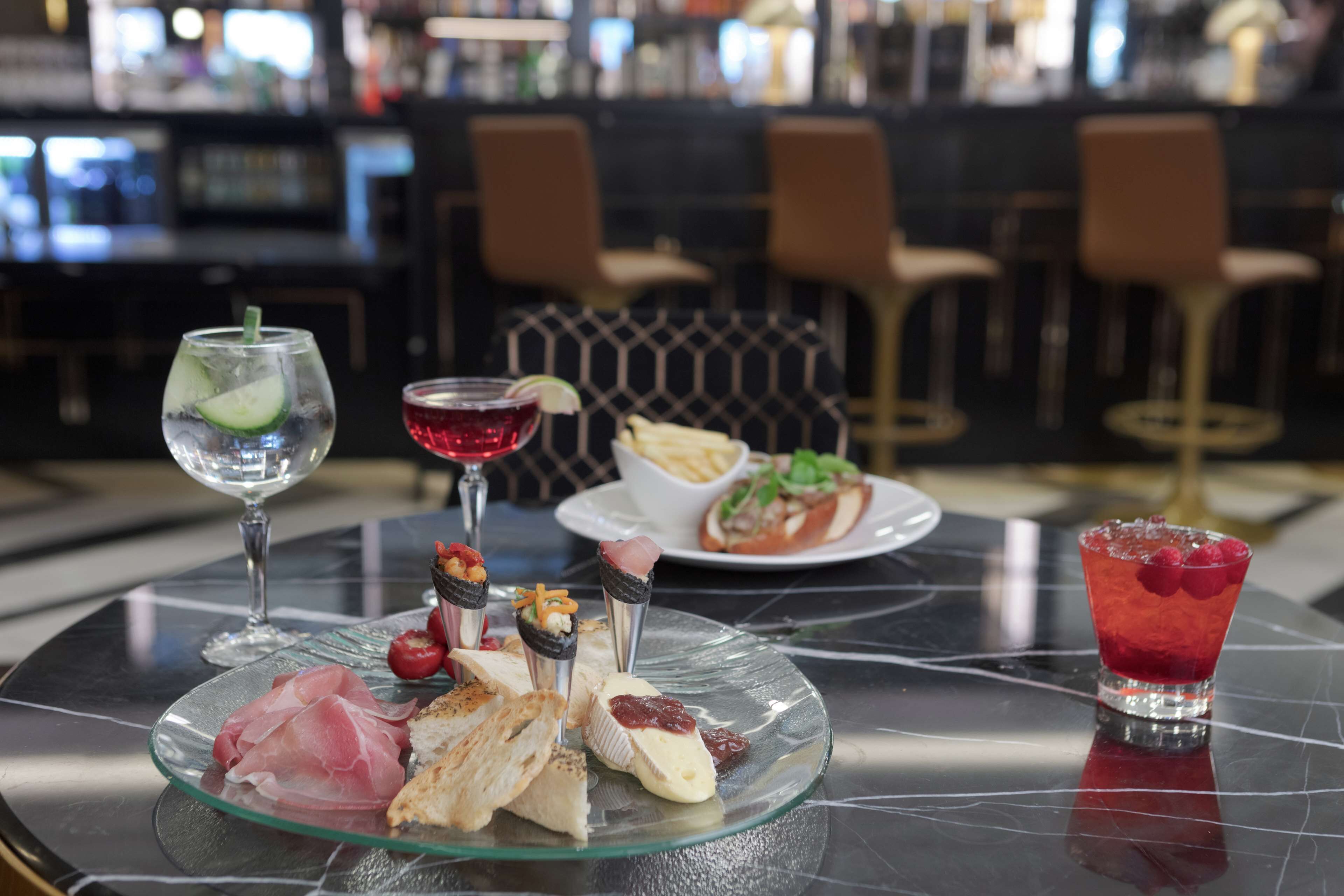 A glass plate with various food items, a glass with a red drink, and a plate with fries and salad on a table in a restaurant.