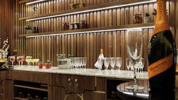 Una zona de bar con paneles de madera, estantes con frascos y una botella de champán.