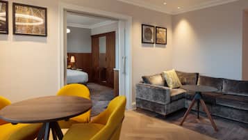 A modern hotel room with a sofa, yellow chairs, a round table, and artwork on the walls.