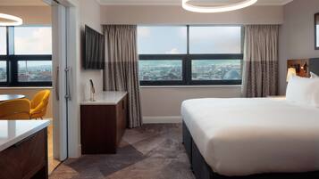 Habitación de hotel con una cama grande, un escritorio, una silla, un televisor y vistas a la ciudad a través de la ventana.