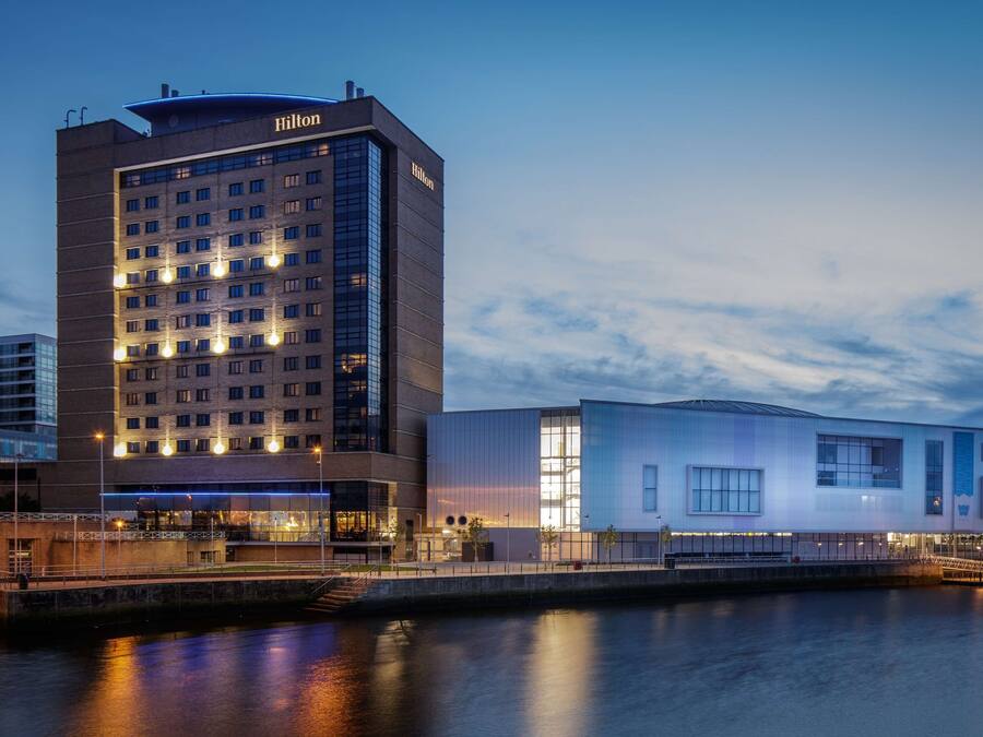 Een modern hotel met een opvallend Hilton-bord, een ligging aan het water en een aangrenzend, eigentijds gebouw.