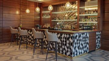 A bar area with a wooden bar counter, multiple stools, and a variety of bottles and glasses.