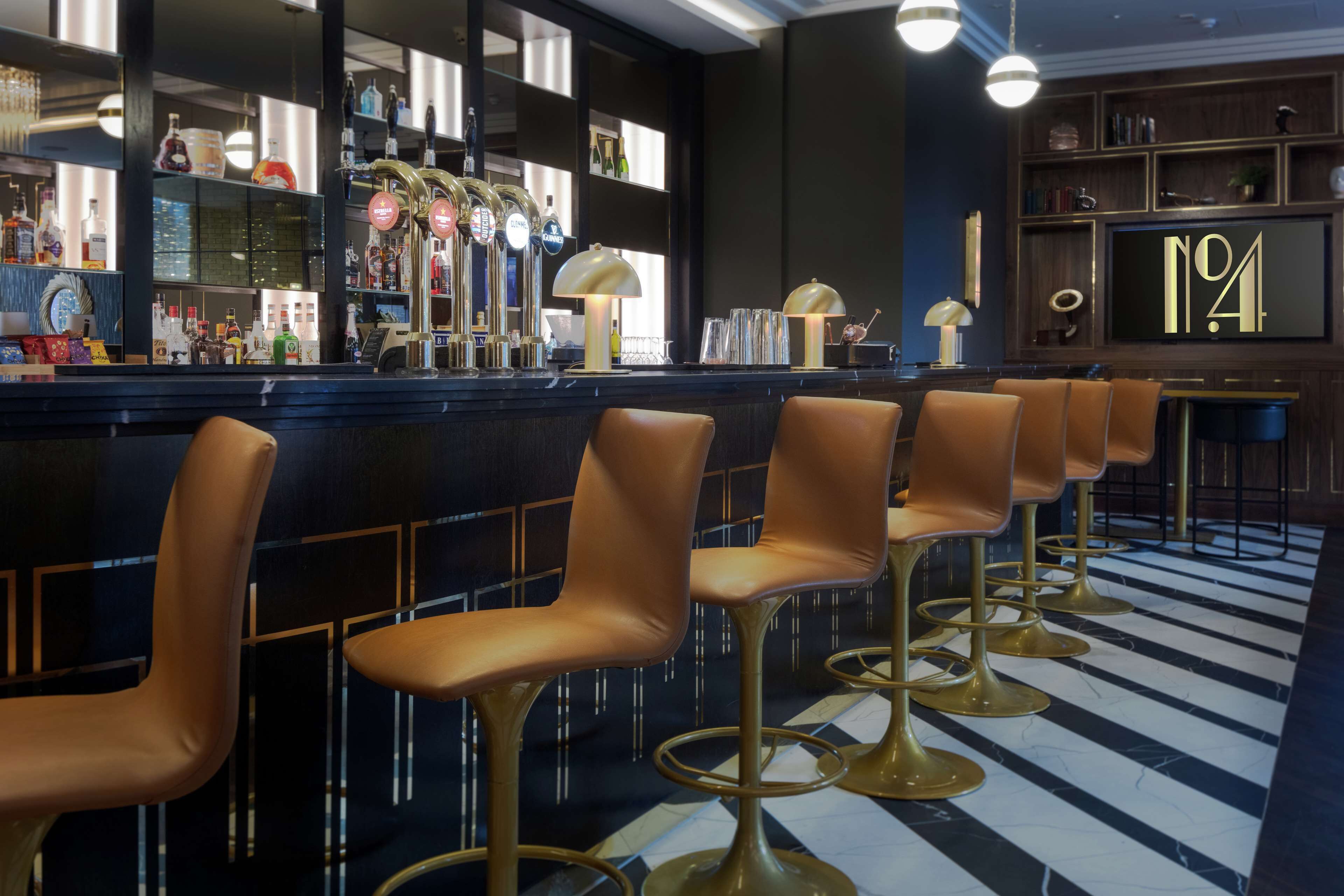 A bar area with multiple stools, a bar counter, and shelves with bottles.