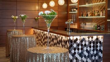 Zona de bar con pared de madera, tres lámparas colgantes y una barra con botellas y vasos.