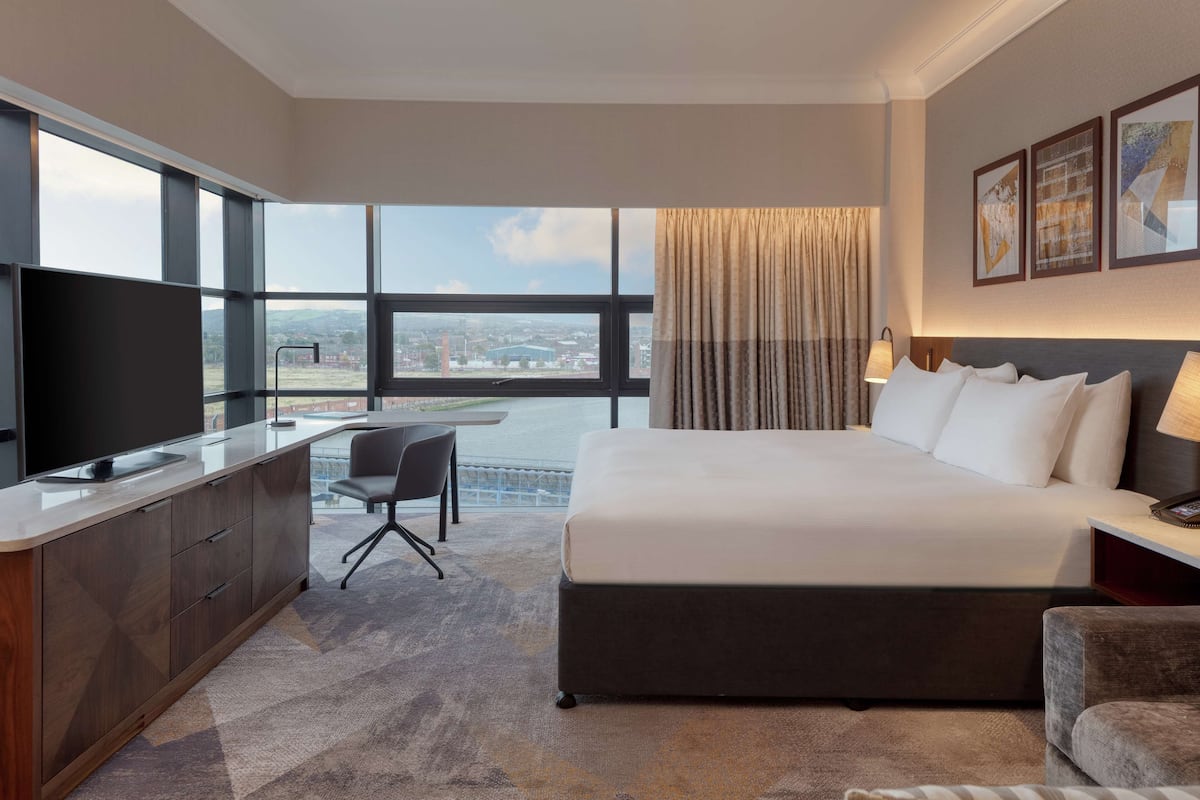 Una habitación de hotel con una cama grande, un escritorio, un televisor y vistas de la ciudad.