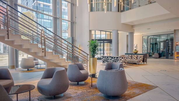 A modern lobby with a staircase, seating area, and large windows.