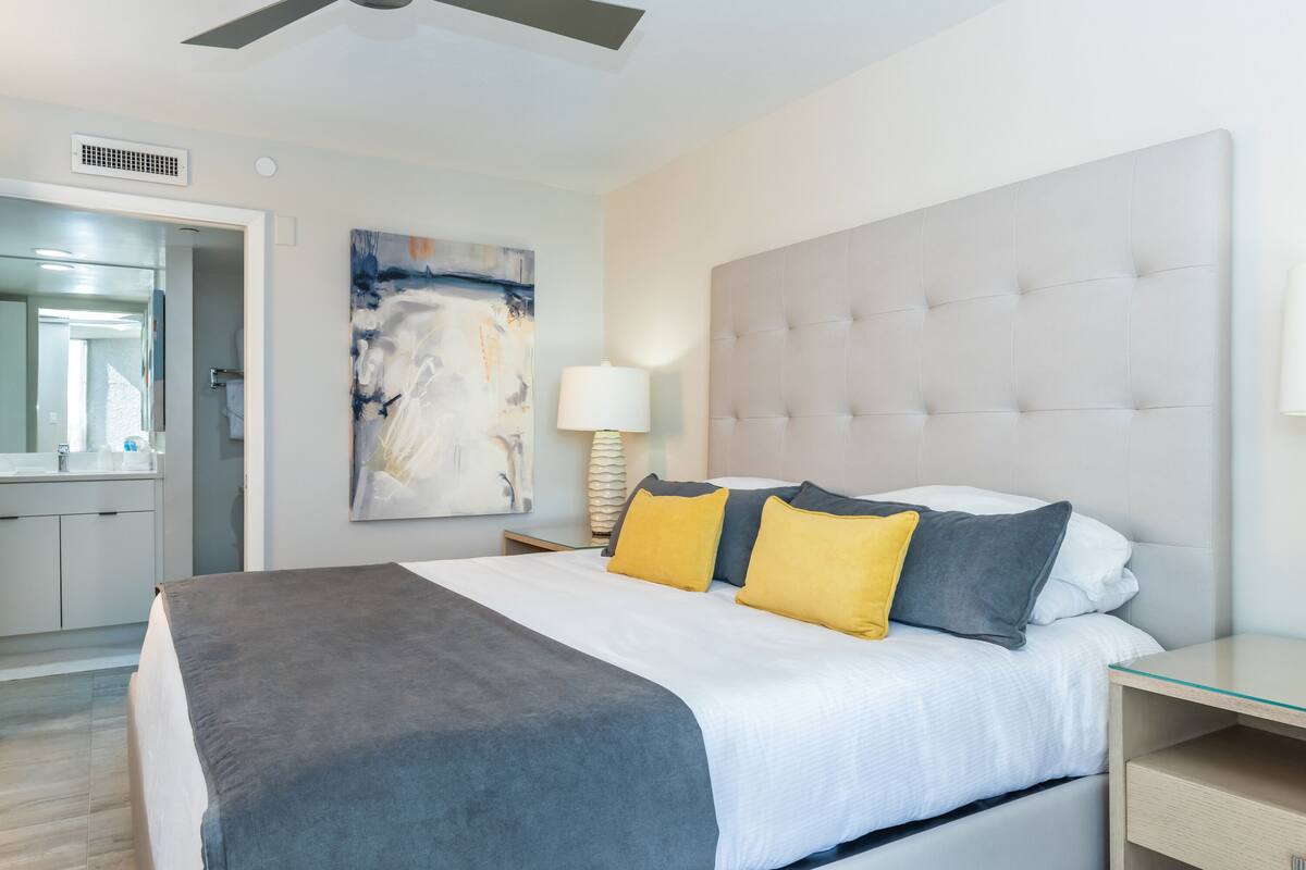 Una habitación de hotel moderna con una cama grande, una mesita de noche, una lámpara y un cuadro en la pared.