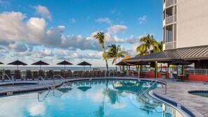 A swimming pool with lounge chairs and umbrellas, surrounded by palm trees and a building with balconies. - DiamondHead Beach Resort (Fort Myers Beach)