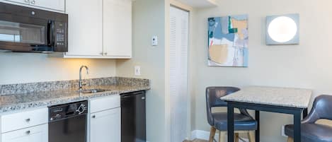 A modern kitchen with white cabinets, a built-in microwave, and a dishwasher. There is a dining area with a table and two chairs.