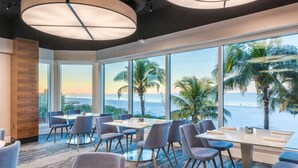 A modern dining area with large windows, a view of the sea, and a tropical setting. - DiamondHead Beach Resort (Fort Myers Beach)