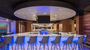 A modern bar area with a central island, bar stools, and a large screen. - DiamondHead Beach Resort (Fort Myers Beach)