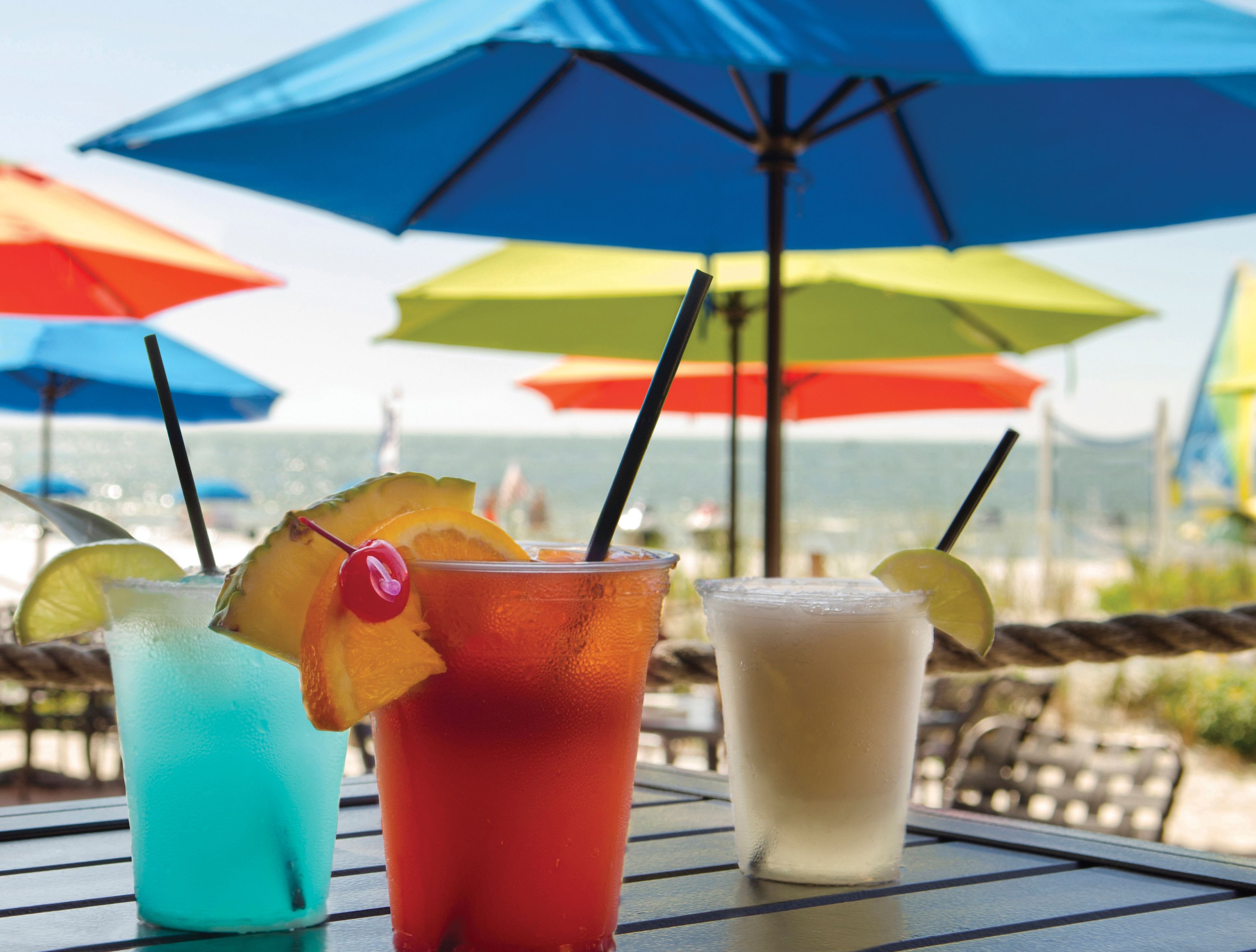 Three drinks on a table with colorful umbrellas in the background.