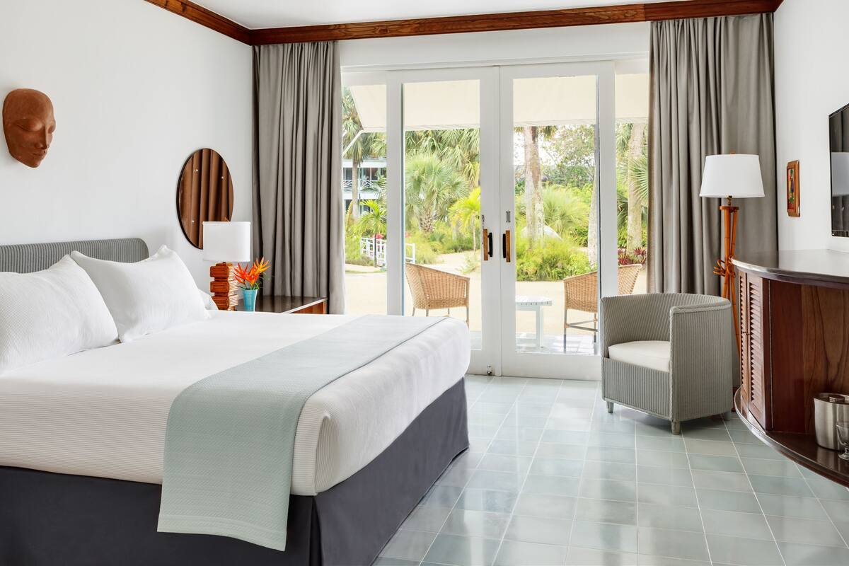 A hotel room with a large bed, a chair, a desk, and a view of the garden through the sliding doors.