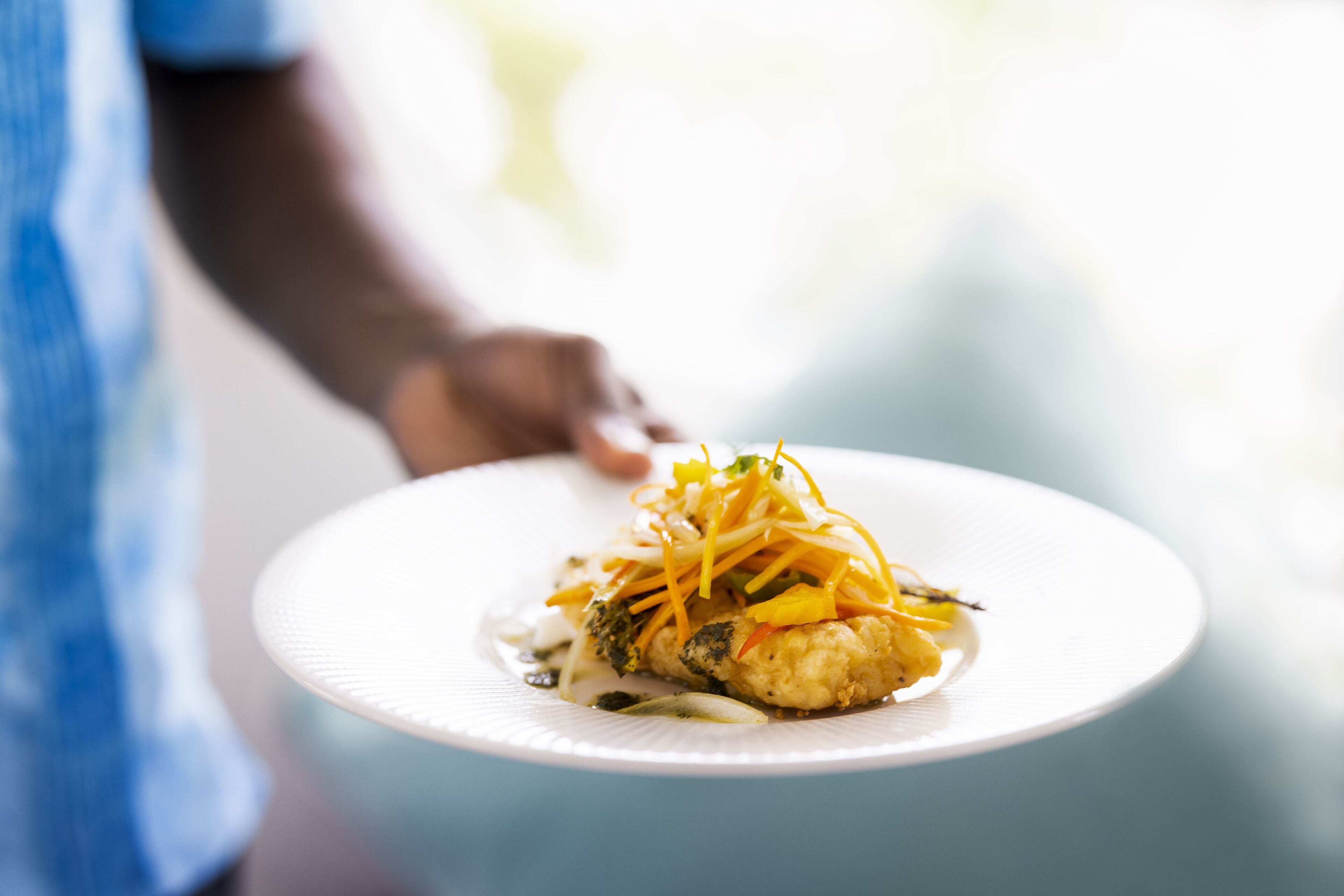 Un plat blanc amb un aliment, possiblement peix, decorat amb verdures grogues i vermelles.