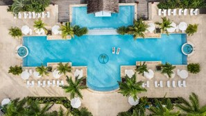 An aerial view of a resort's swimming pool area with multiple lounge chairs and palm trees.