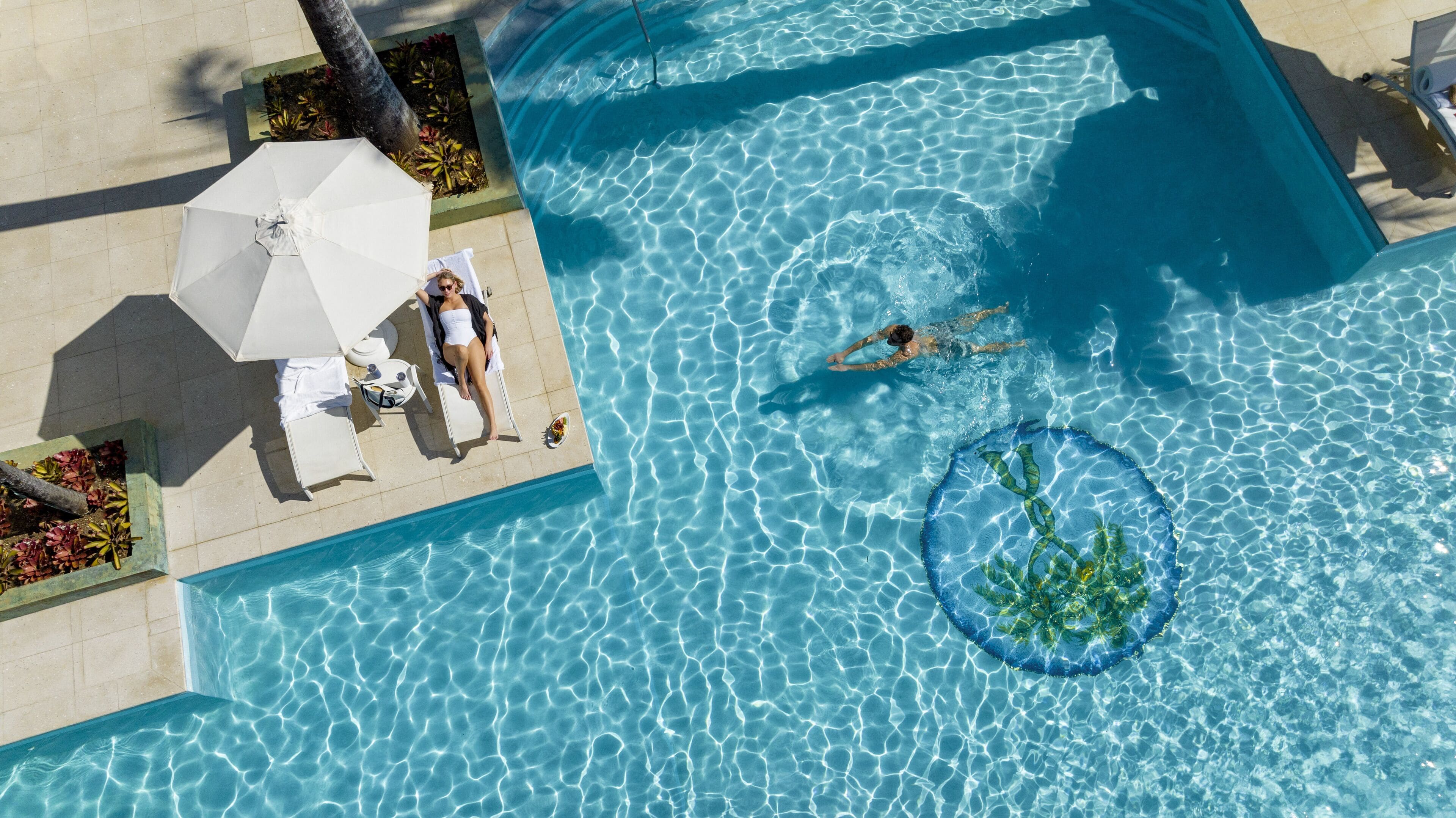 Vista aérea de una piscina con agua cristalina, sillas de descanso y una sombrilla.