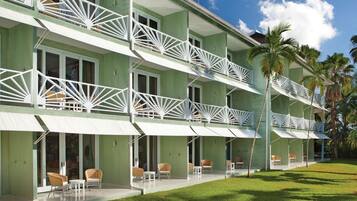 A hotel with a green facade, white balconies, and outdoor seating areas.