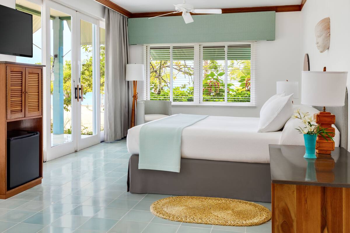 A bedroom with a bed, a TV, a desk, and a window with blinds.