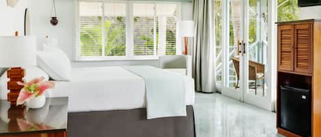 A bedroom with a bed, a desk, a lamp, a TV, and a sliding glass door leading to a balcony.