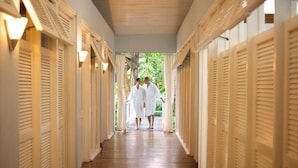 A corridor with wooden flooring and white doors with shutters, leading to an outdoor area with greenery. - Couples Negril All Inclusive (Negril)