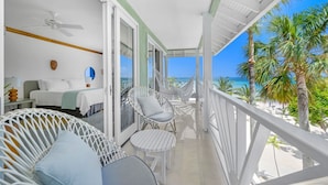 A balcony with white wicker furniture, a bed with white bedding, and a view of the beach and ocean. - Couples Negril All Inclusive (Negril)