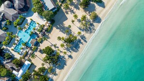 An aerial view of a beach resort with a swimming pool, sun loungers, and palm trees. - Couples Negril All Inclusive (Negril)