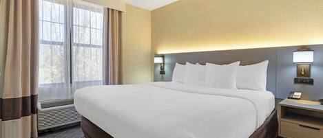 A hotel room with a large bed, a bedside table with a lamp, a heater, and a window with curtains.