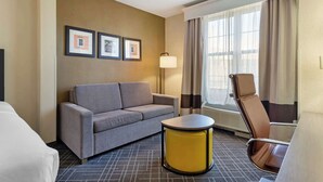 Habitación de hotel con sofá, una pequeña mesa redonda, una silla, una lámpara y cuadros en la pared.