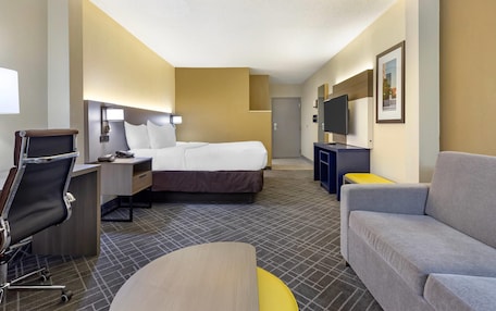A hotel room with a bed, desk, chair, sofa, TV, and a framed picture on the wall.