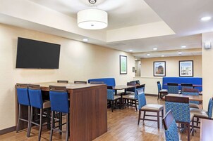 Un comedor de hotel con una larga barra, taburetes azules y varias mesas con sillas.