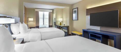 A hotel room with two beds, a TV, a desk, and a window with curtains.