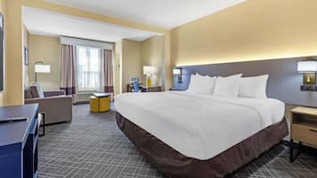 A hotel room with a large bed, a desk, a chair, and a sofa.