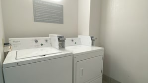 A laundry room with Whirlpool brand washers and dryers, a sign with laundry guidelines, and a wall-mounted light. - Red Roof Inn Winston-Salem (Winston-Salem)