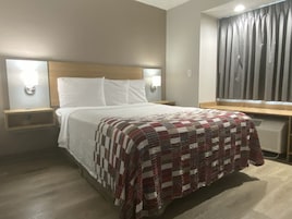 Una habitación de hotel con una cama, dos mesitas de noche con lámparas, una ventana con cortinas y un radiador.