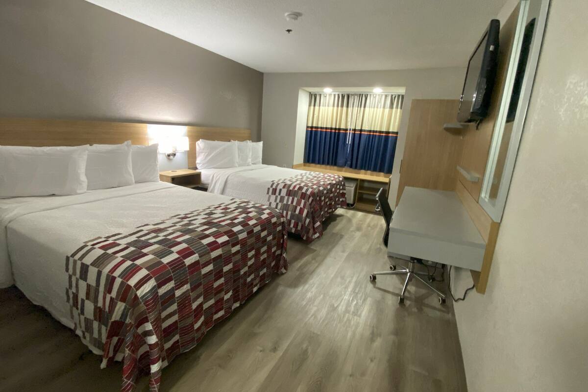 A hotel room with two beds, a desk, a chair, a TV, and a window with curtains.